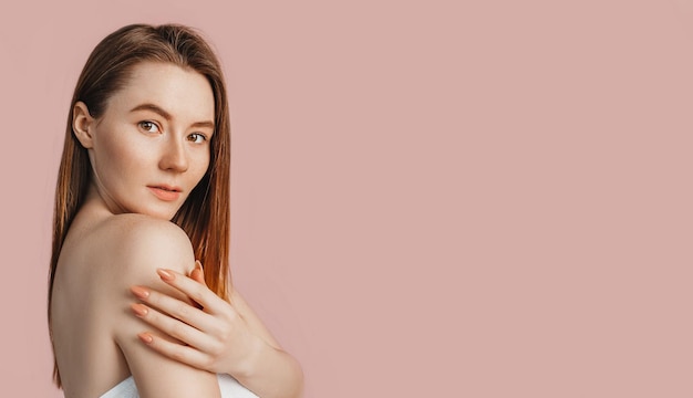 Beautiful sensual young girl with clean skin on a pink background with a mockup Topless woman in a towel The concept of spa treatments natural beauty and care youth cream and mask freshness
