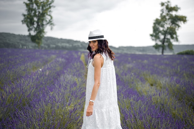 Bella giovane donna sensuale con cappello e abito bianco sul campo di lavanda