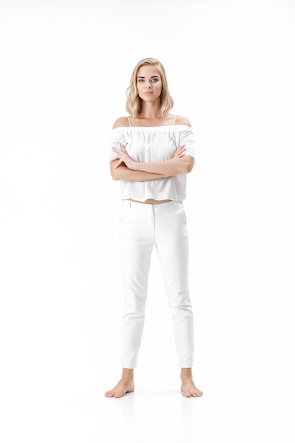 Photo beautiful serious blond woman in a white blouse and pants on a white background