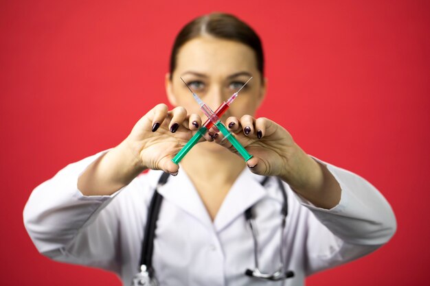 Beautiful serious doctor holding two crossed syringes with red and white liquids