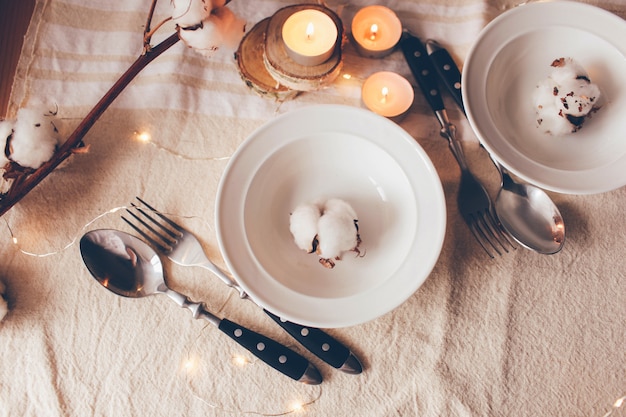 Bellissimo tavolo servito con decorazioni, candele e ramo di cotone sulla tovaglia di lino. tabella servita per il pranzo di primavera in salotto. vista da vicino, impostazione della tabella. decorazioni primaverili.