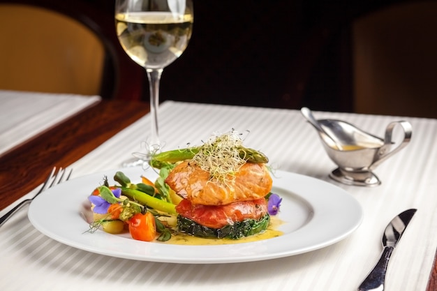 Beautiful serving dishes in the restaurant, red fish salmon with vegetables on a white plate in a restaurant on a black background with white wine stokanom