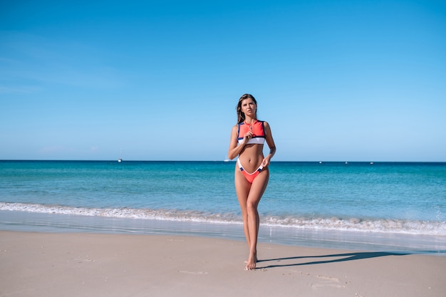 赤い水着のビーチでポーズ美しいセクシーなブルネットの少女。夏休み