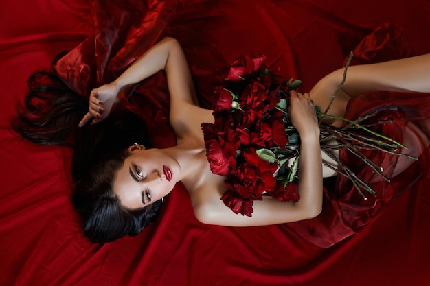 바닥에 누워있는 빨간 장미 꽃다발, 벗은 신체 부위, 여성의 에로틱 한 초상화와 함께 아름 다운 섹시 한 갈색 머리