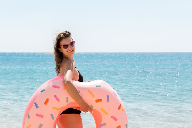 Красивая сексуальная милая счастливая женщина на пляже с розовым резиновым надувным кольцом в руке. Летние каникулы и концепция отпуска.