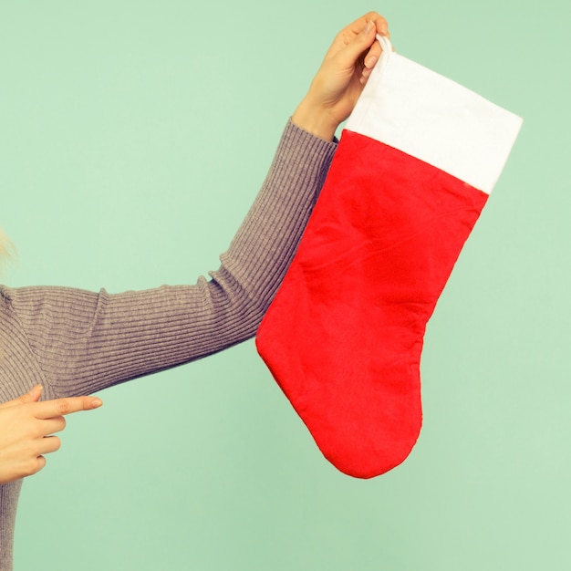 Una bella ragazza sexy con un cappello di capodanno e un vestito grigio punta il dito contro un calzino di natale. celebrazione di natale o capodanno