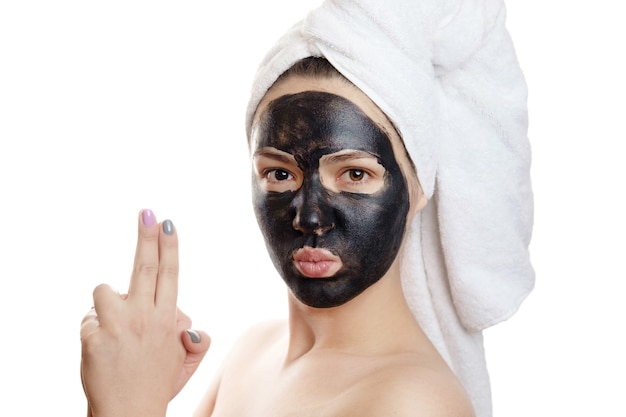 Photo beautiful sexy girl with black face mask on the white background, close-up portrait, isolated, girl with a towel on her head, black mask on girl's face, is indulging, like a criminal