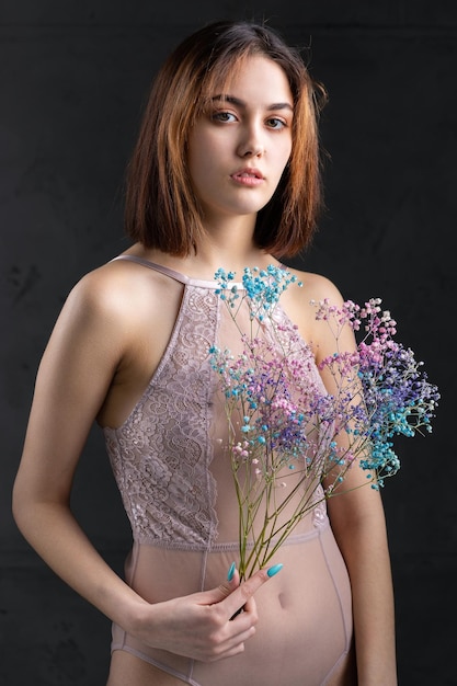 우아한 누드 바디수트를 입은 아름다운 섹시한 여성이 손에 꽃을 들고 스튜디오에서 패션 모델 소녀의 패션 뷰티 초상화
