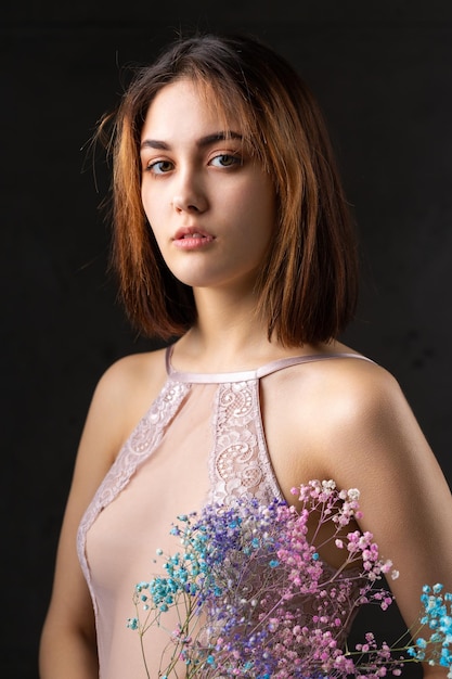 A beautiful sexy lady in an elegant nude bodysuit holds flowers in her hands Fashion beauty portrait of fashion model girl in studio