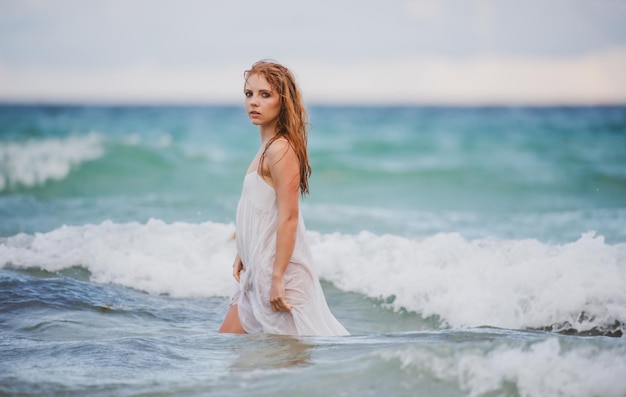 열 대 해변에서 아름 다운 섹시 한 여자 바다에서 젊은 여자 바다 또는 바다에서 따뜻한 바다 물을 즐기는 그을린 관능적 인 소녀 젖은 섹시 드레스
