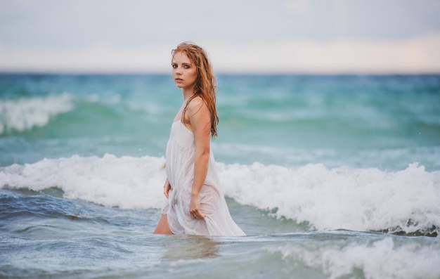 Beautiful sexy woman on tropical beach Young woman at sea Tanned sensual girl in enjoying warm ocean water on sea or ocean Wet sexy dress