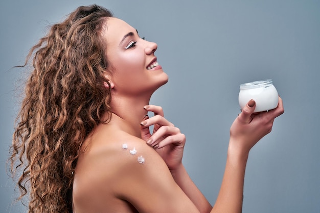 Beautiful sexy woman with fresh health skin applying cream on shoulder Isolated on grey background Side view