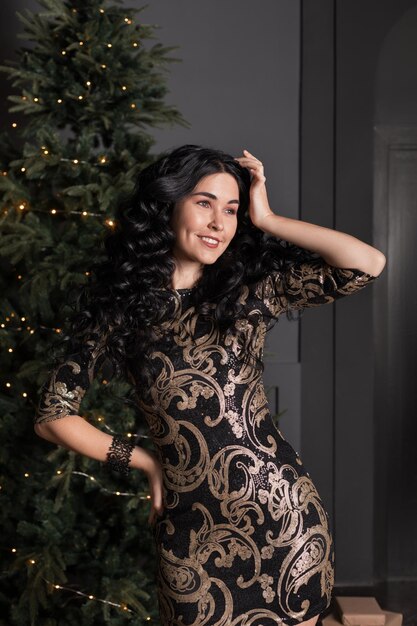 写真 クリスマス ツリーの近くに立っている長い巻き毛を持つ美しいセクシーな女性
