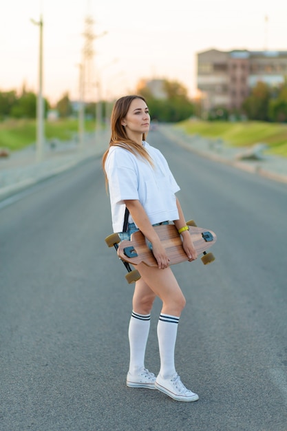 Beautiful sexy young girl in short shorts walking with longboard in sunny weather. Leisure. Healthy lifestyle. Extreme sports. Fashion look, outdoor hipster portrait, Bali, sneakers,hipster,sunse