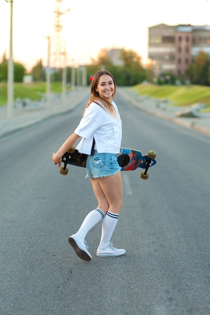 Beautiful sexy young girl in short shorts walking with longboard in sunny weather