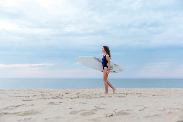 Beautiful sexy young surfer girl walking on the beach