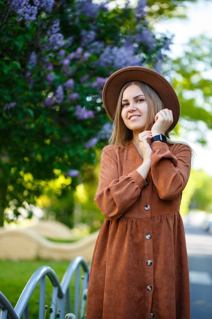 Beautiful shapely long-haired girl in the hat on a background of lilac flowers