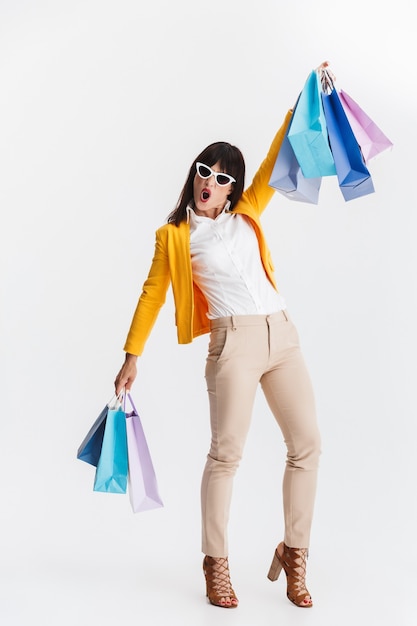 beautiful shocked young business woman posing isolated over white wall holding shopping bags.