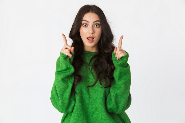 beautiful shocked young woman dressed in green sweater posing isolated on white wall pointing have an idea.