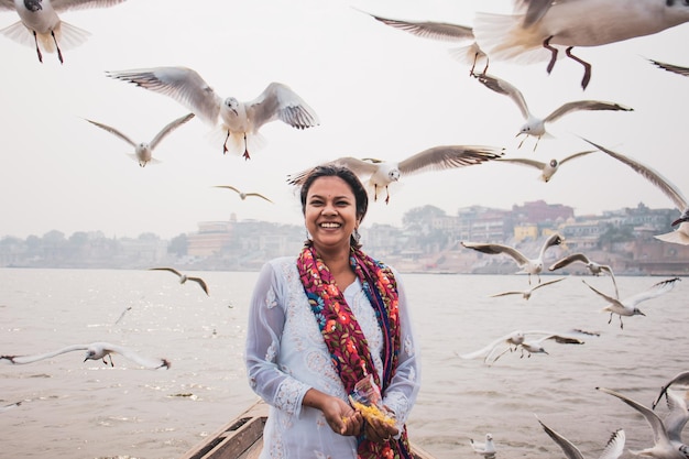 Beautiful shot of a happy Indian woman feeding birds flying around her on a beach