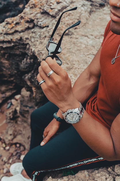 Beautiful shot of a young man holding his sunglasses while sitting on the rocks