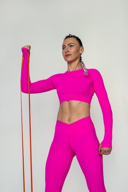 Beautiful shot of young woman in pink sportswear doing exercises with resistance band isolated on white background sport as a healthy lifestyle athletic body