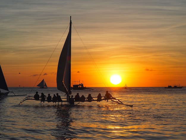 Beautiful silhouette of sunset in the sea and travellers on sailboat at Boraycay Philippin