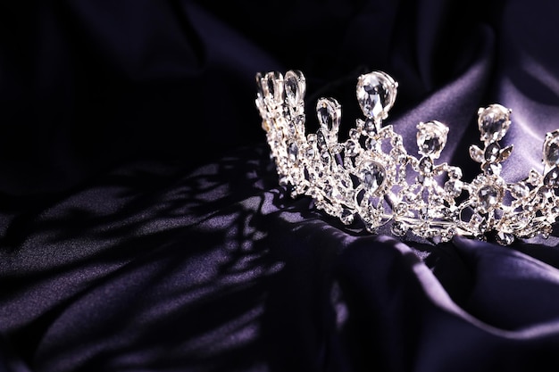 Beautiful silver tiara with diamonds on dark cloth Space for text
