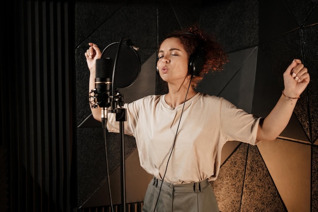 Beautiful singer girl in headphones sensually singing working on new music album in sound recording studio