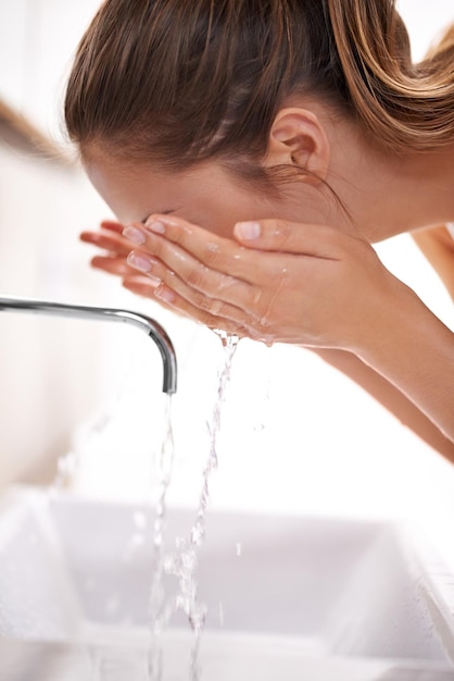 Beautiful skin begins with washing Closeup shot of a young woman washing her face over a sink