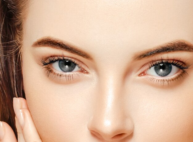 Beautiful skin woman with healthy hair and beauty eyes lashes and lips touching her face by fingers. Studio shot.