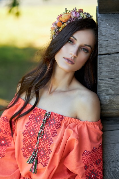 Photo beautiful slavic woman in an orange ethnic dress and a wreath of flowers on her head. beautiful natural makeup