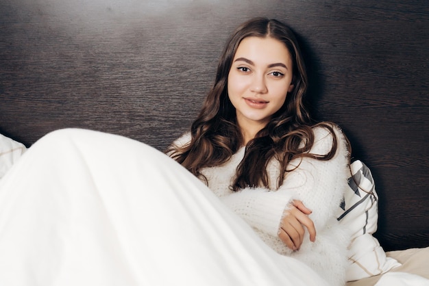 Beautiful sleepy girl in white pajamas lies in bed early in the morning and does not want to get up