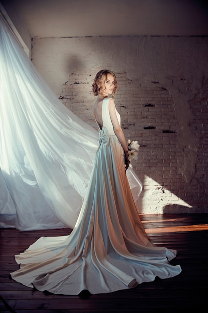 Beautiful slender blonde in the evening sun in a long white dress.