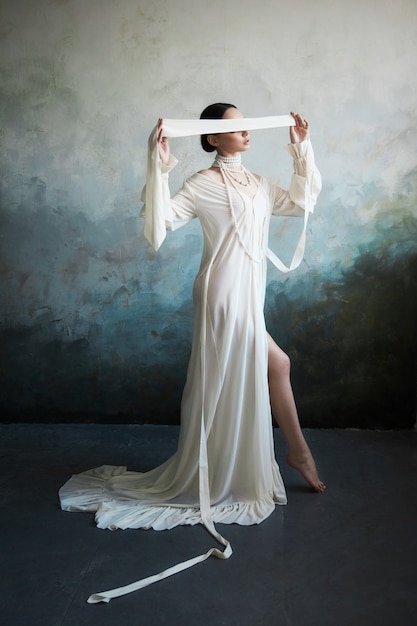 Красивая стройная брюнетка сидит на диване в длинном белом платье