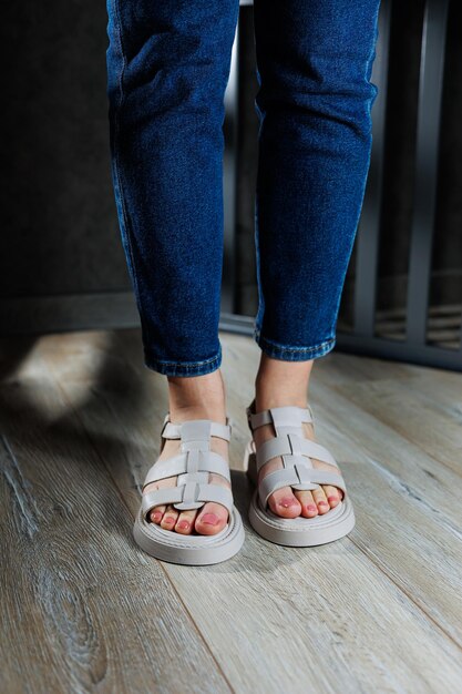 Beautiful slender female legs in leather sandals on the floor against gray parquet Collection of women's sandals