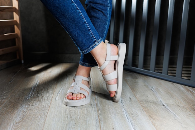 Beautiful slender female legs in leather sandals on the floor against gray parquet Collection of women's sandals