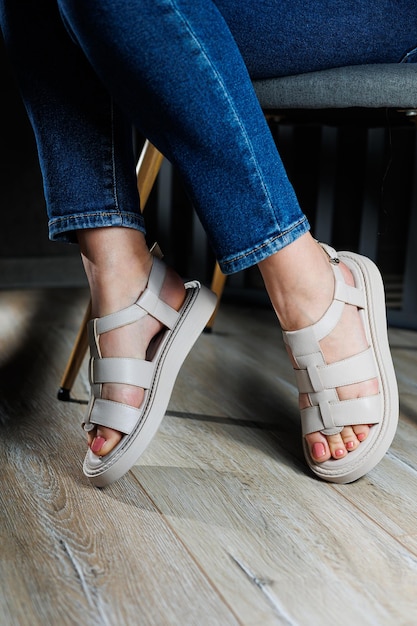 Beautiful slender female legs in leather sandals on the floor against gray parquet Collection of women's sandals