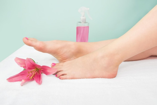 Beautiful slender female legs spray bottle with pink liquid and rose flower The concept of cosmetology shugaring Cropped photo of female legs