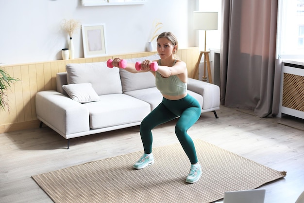 La bella donna sottile di forma fisica si accovaccia con i dumbbells. sport, stile di vita sano. la ragazza fa sport a casa.