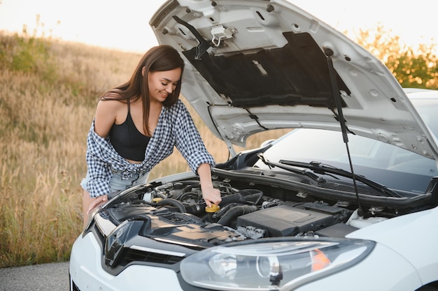 シャツとショートパンツを着た美しいスリムな女の子が道路の開いた車のフードに見えます