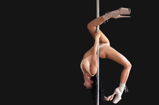 Beautiful slim girl with a pylon. Female pole dancer woman dancing on the pole on a black background. Isolated black background