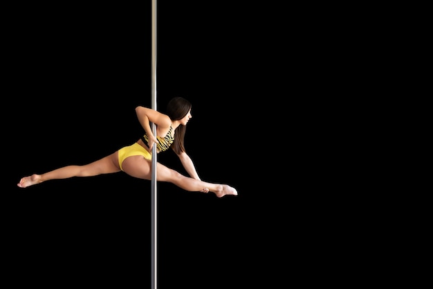 Beautiful slim girl with a pylon. Female pole dancer woman dancing on the pole on a black background. Leg-split. Isolated black background