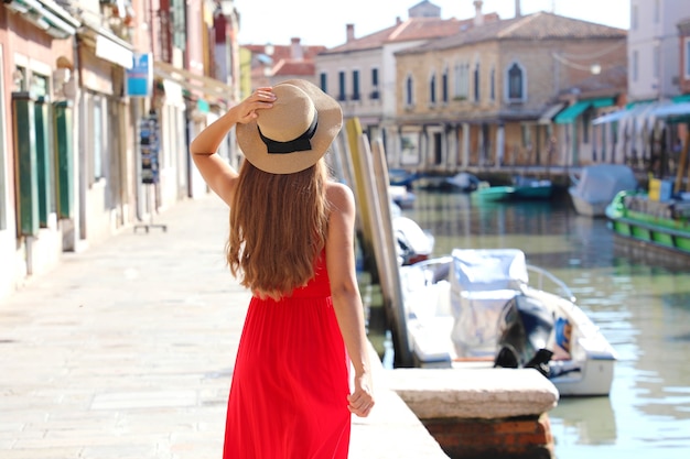 Foto bellissimo modello slim con vestito rosso e cappello che cammina a murano, venezia