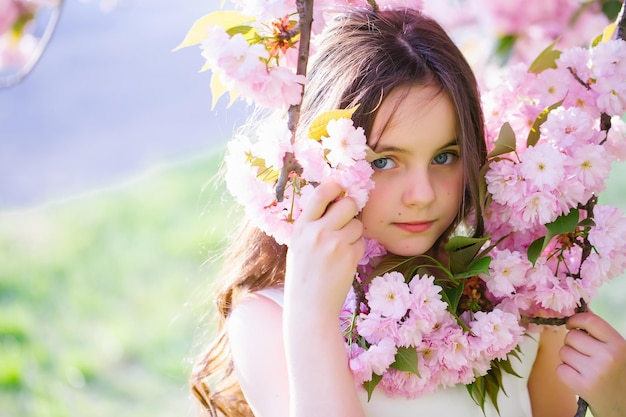 Photo beautiful small girl in white glamour dress with long hair and smiling face in spring pink flower bl