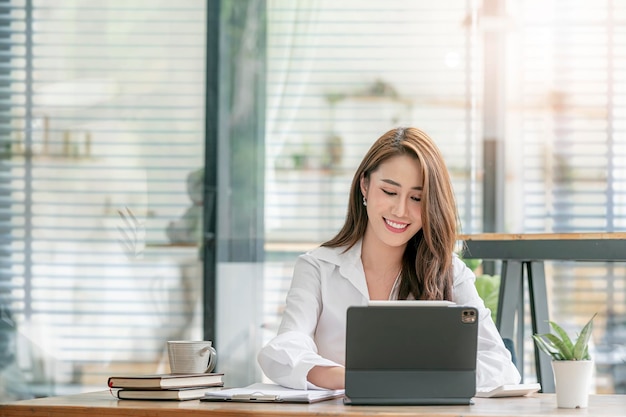 Photo beautiful smiley asian woman working on portable tablet with happiness while sitting in modern office room, successful business concept.