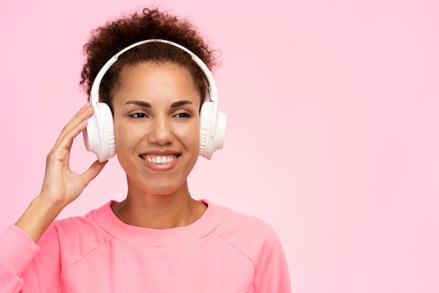 Beautiful smiling African American woman listening music in headphones isolated on pink background