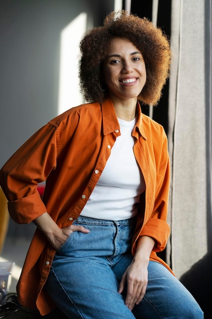 Beautiful smiling African American woman wearing casual orange t shirt jeans sitting at home