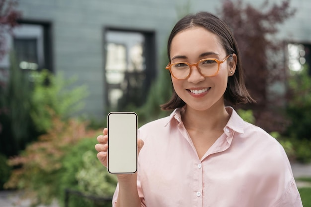 Beautiful smiling asian woman holding mobile phone shopping online, showing digital screen, mock up