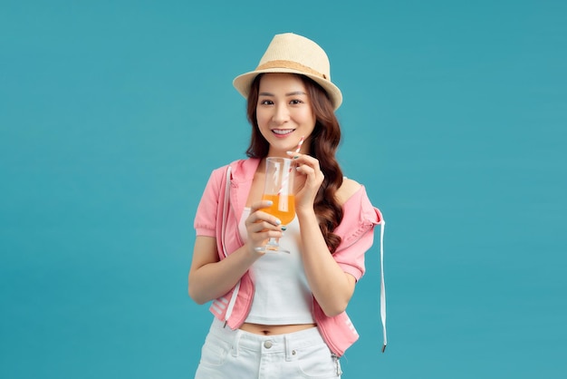 Beautiful smiling Asian woman with a glass of orange juice isolated on colorful blue background